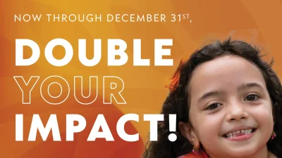 The image features a vibrant orange background with text stating "Now through December 31st, Double Your Impact!" alongside the smiling face of a young girl with curly hair and an orange bow, symbolizing a fundraising or charitable campaign. It conveys warmth, positivity, and urgency for action before the year's end.